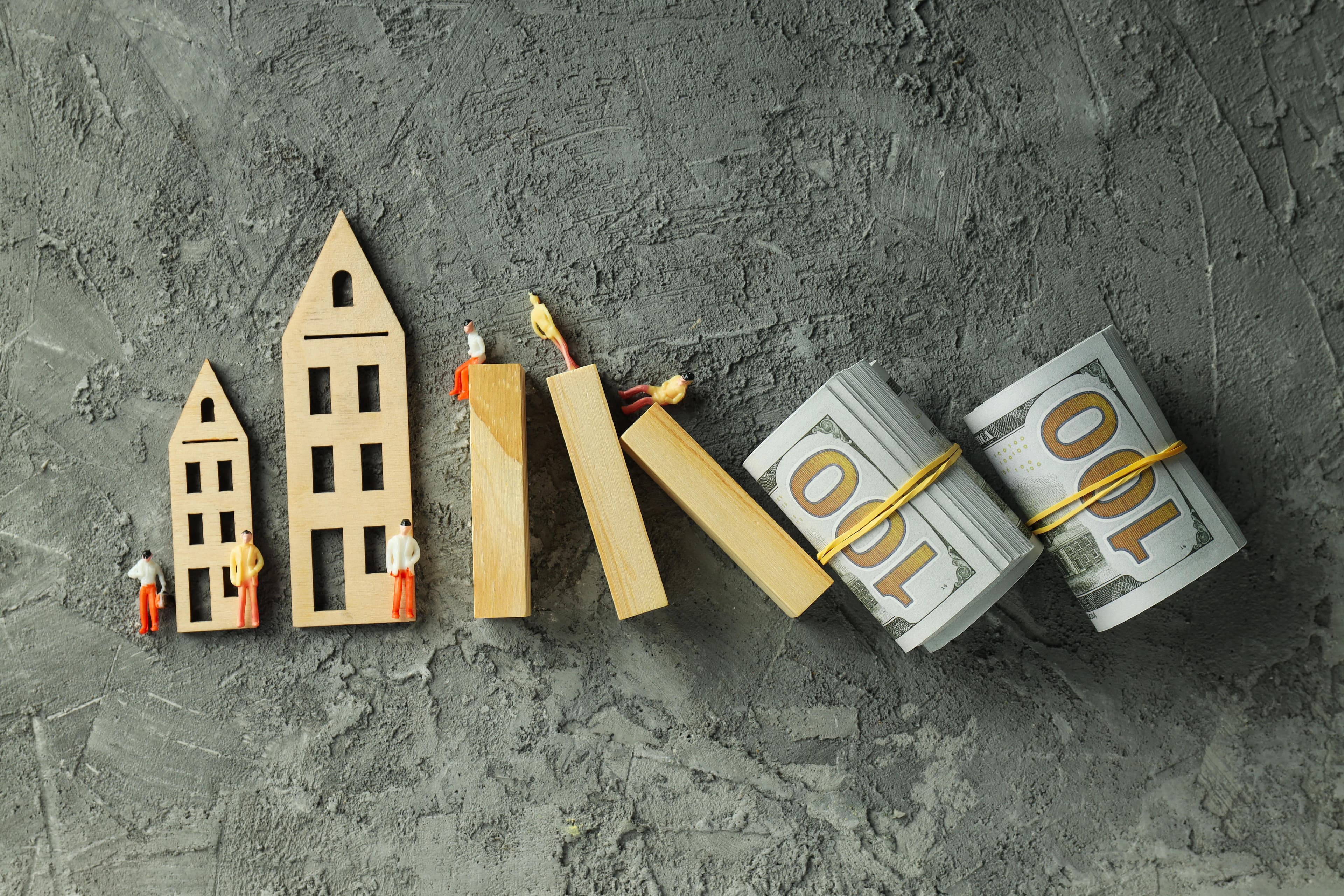 Wooden scale models next to two bundles of dollar bills